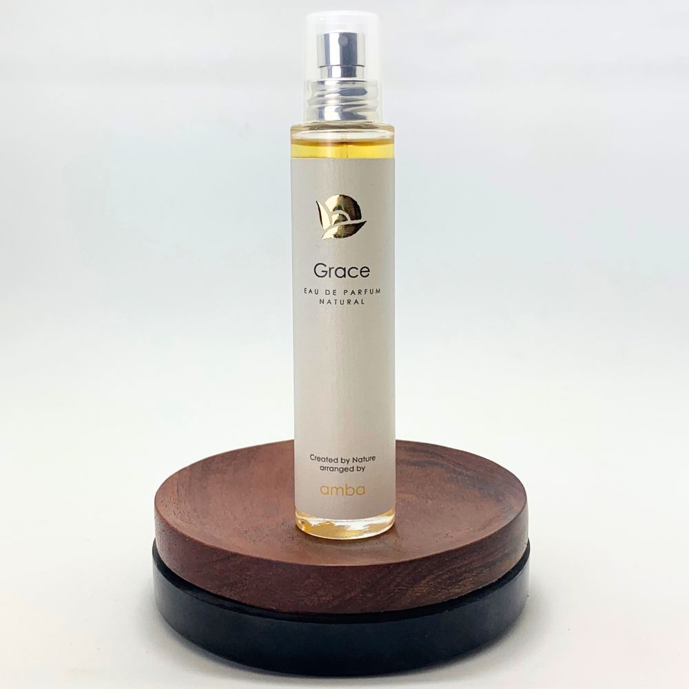 Flasche Naturparfüm Grace von amba auf braunem Holzsockel vor hellem Hintergrund