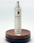 Flakon von amba „Existence“ Naturparfum auf Holzsockel vor weißem Hintergrund