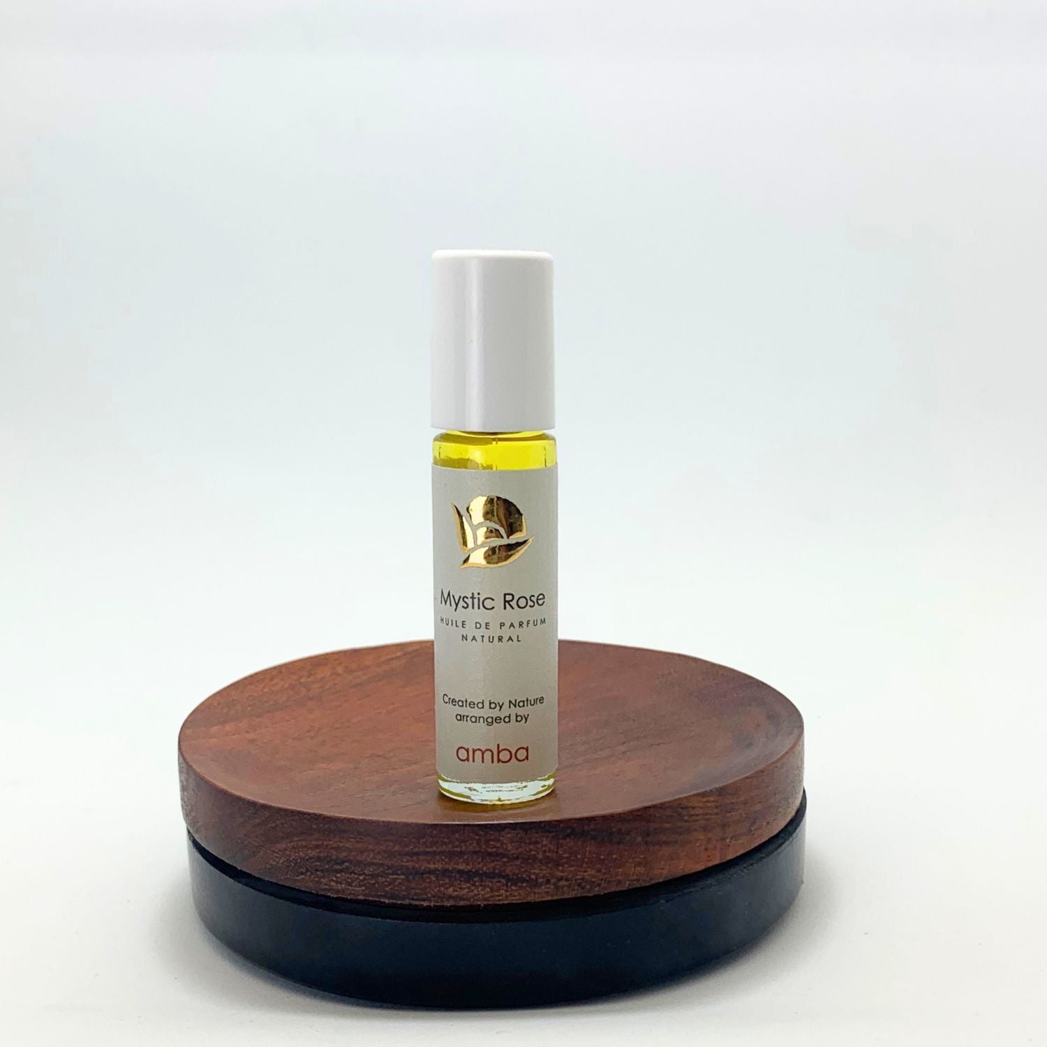 Roll-on des Mystic Rose Naturparfums von amba auf Holzsockel vor weißem Hintergrund