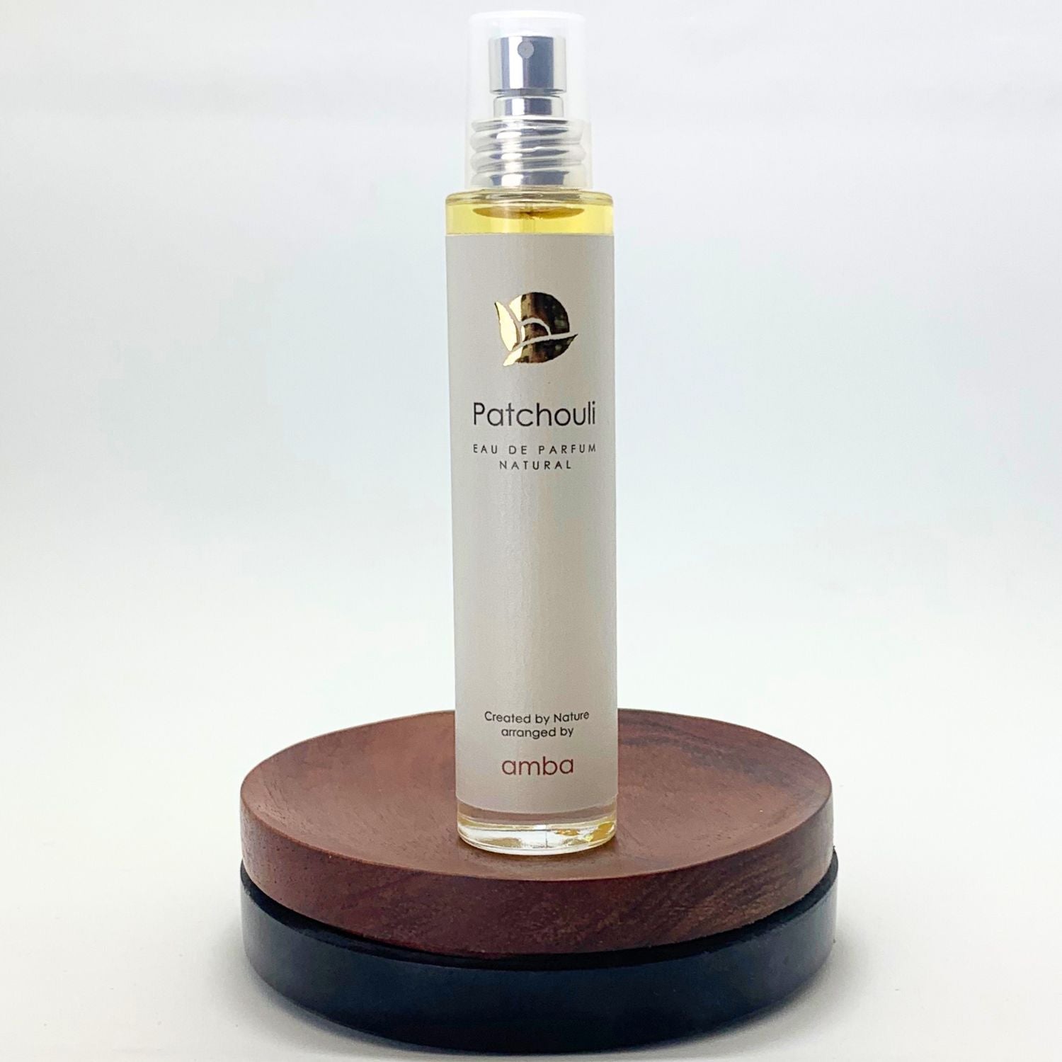 Flakon Patchouli Naturpafrüm von amba auf Holzsockel und vor weißem Hintergrund.