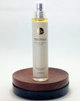 Flakon Patchouli Naturpafrüm von amba auf Holzsockel und vor weißem Hintergrund.