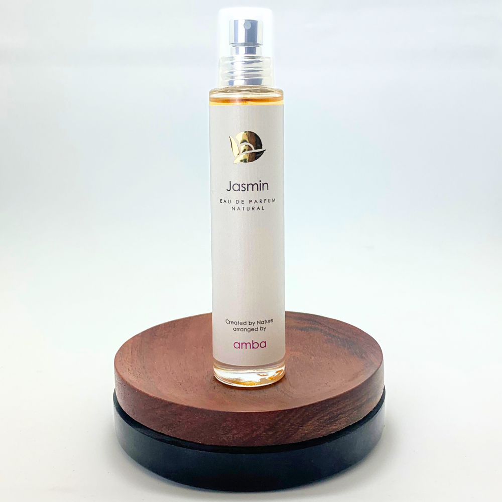 Flasche Naturparfüm Jasmin von amba auf braunem Sockel vor hellem Hintergrund